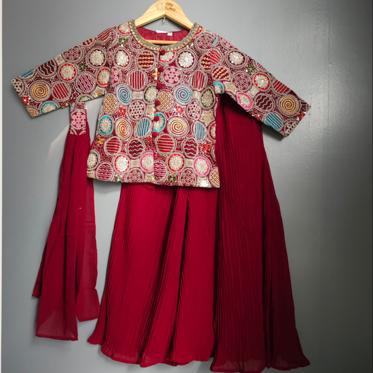 Traditional outfit with embroidered top and red skirt on a gray background