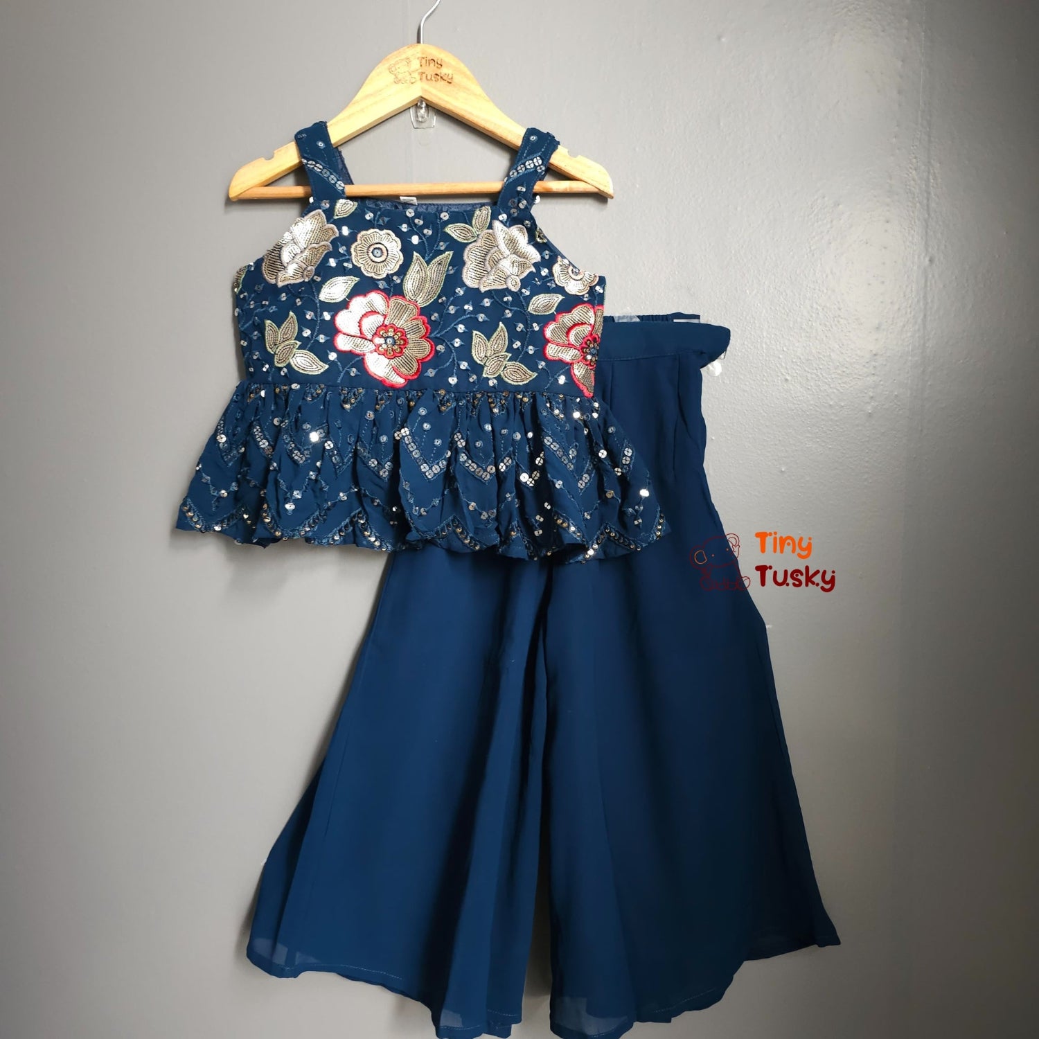 Blue floral top and pants set on a hanger against a gray background