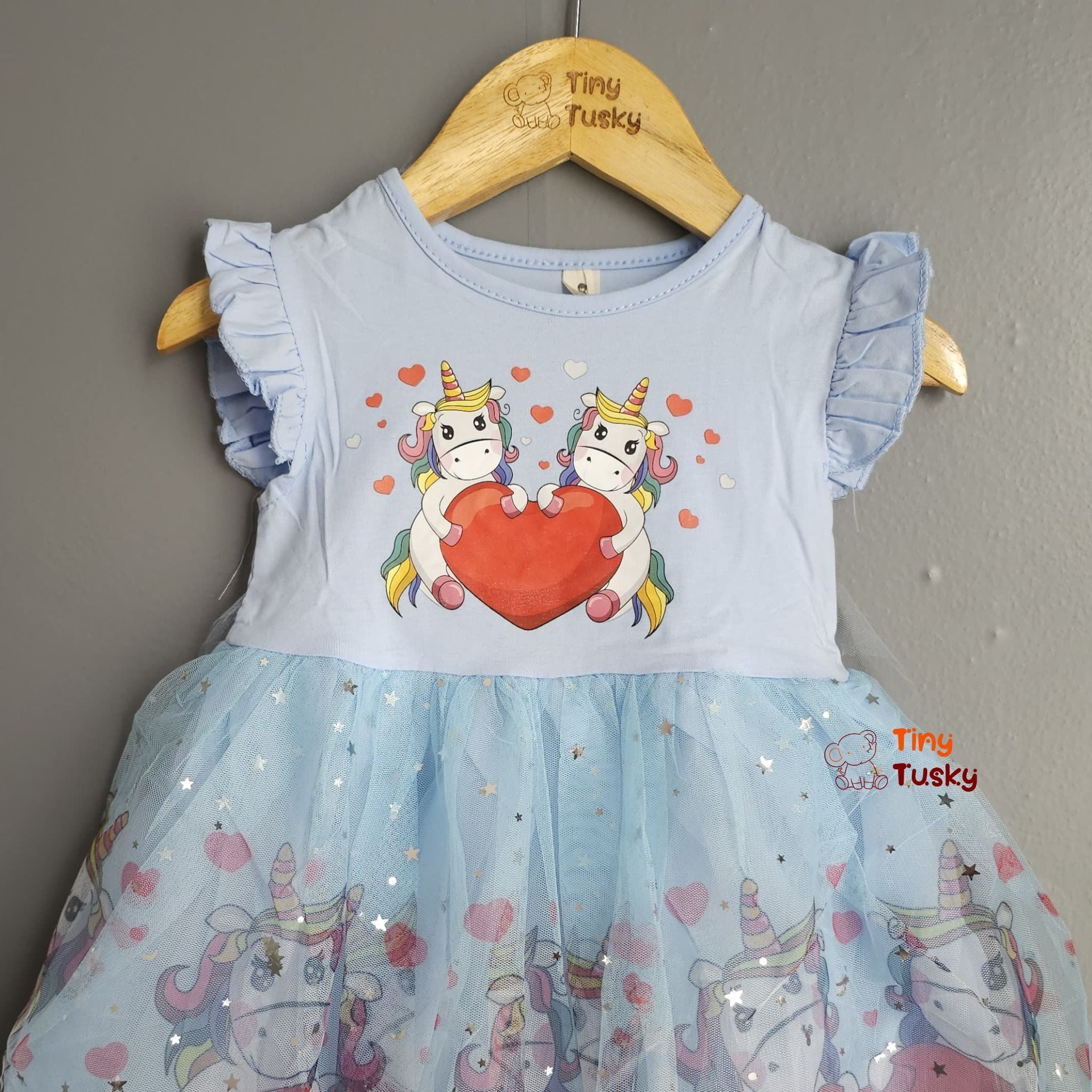 Children's dress with unicorn design on a hanger against a gray wall.