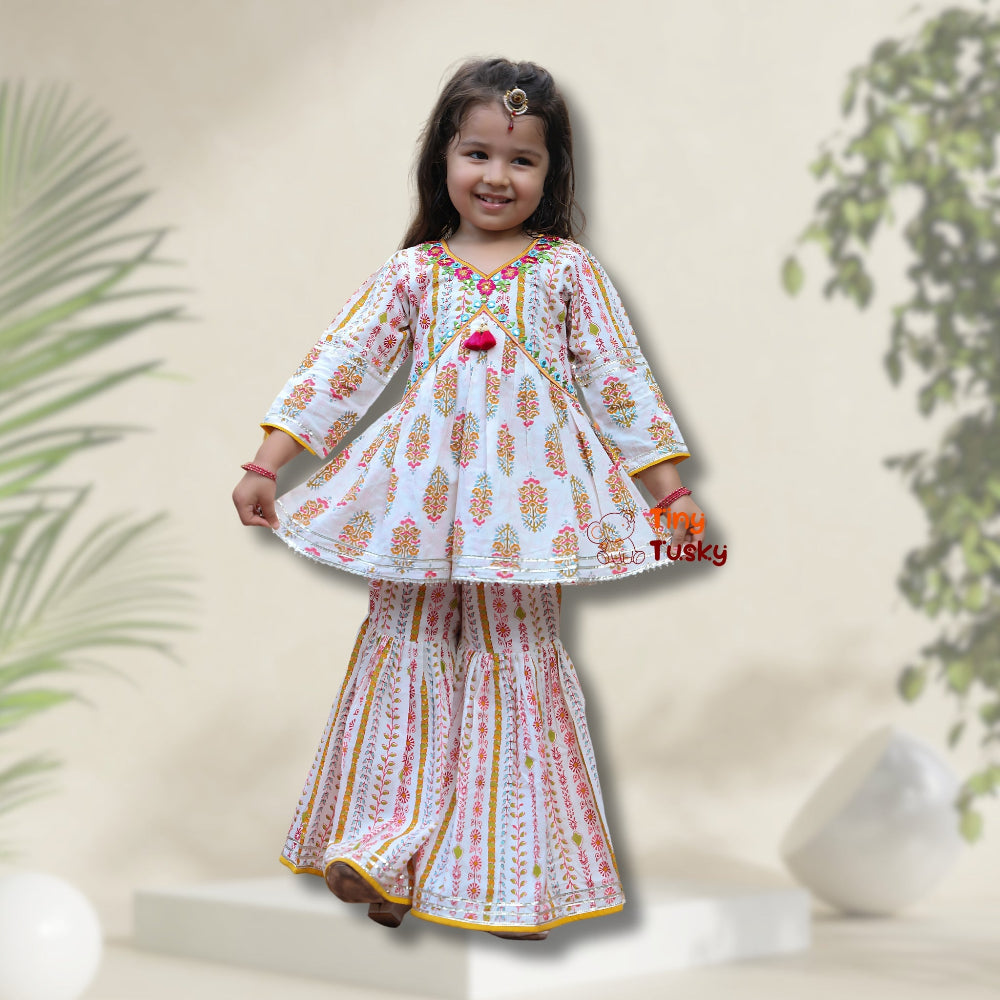Young girl wearing a white traditional outfit with colorful patterns against a neutral background