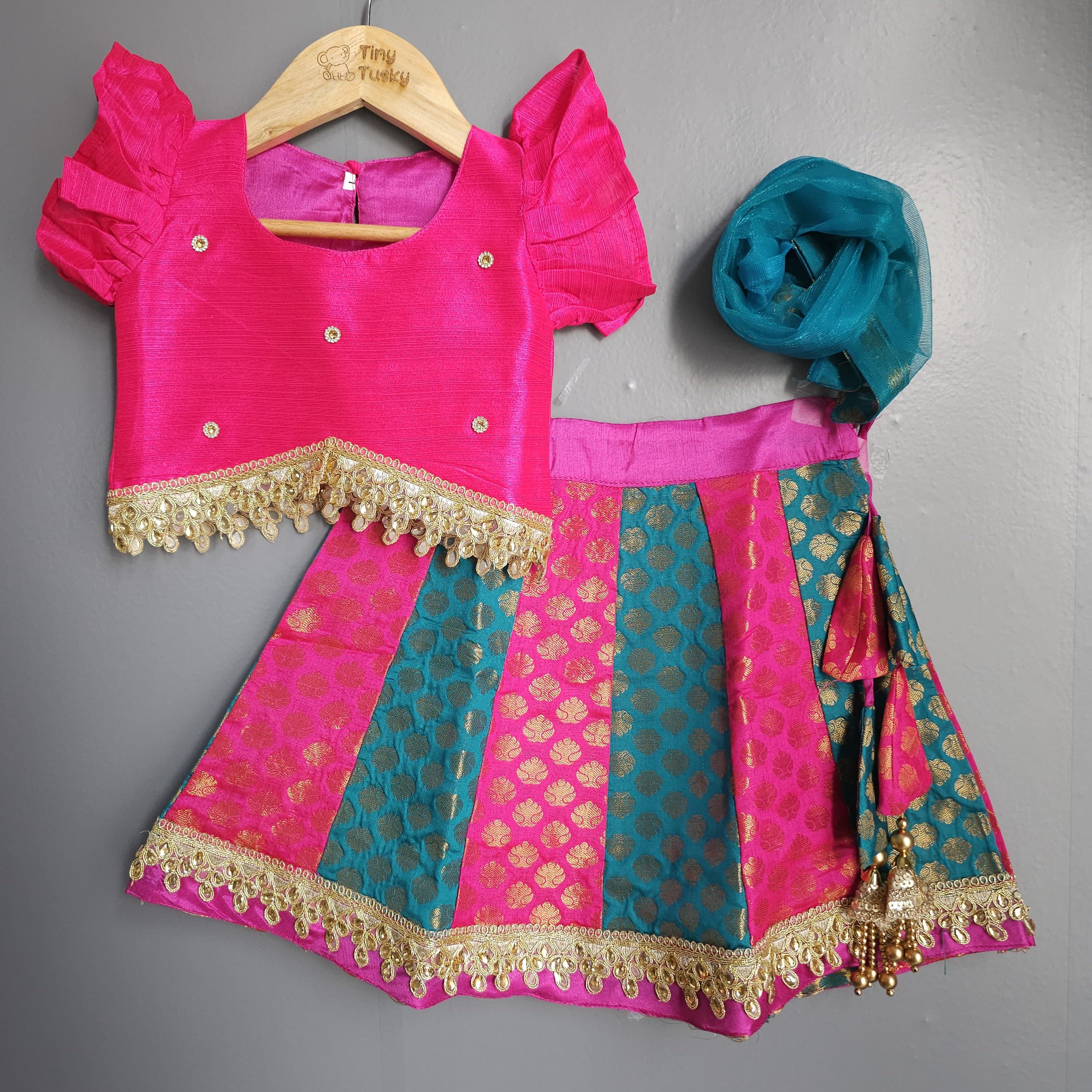 Pink and teal traditional outfit with a matching dupatta on a gray background